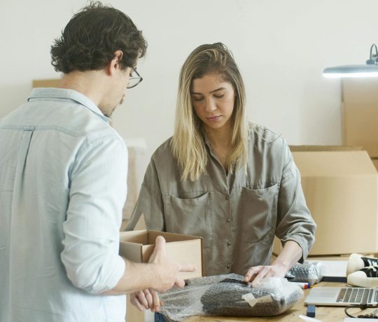 pexels-photo-7289711-7289711 Two young adults packing clothing items in an office for their online store startup.